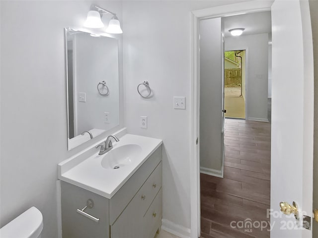 half bathroom featuring vanity, baseboards, toilet, and wood finished floors