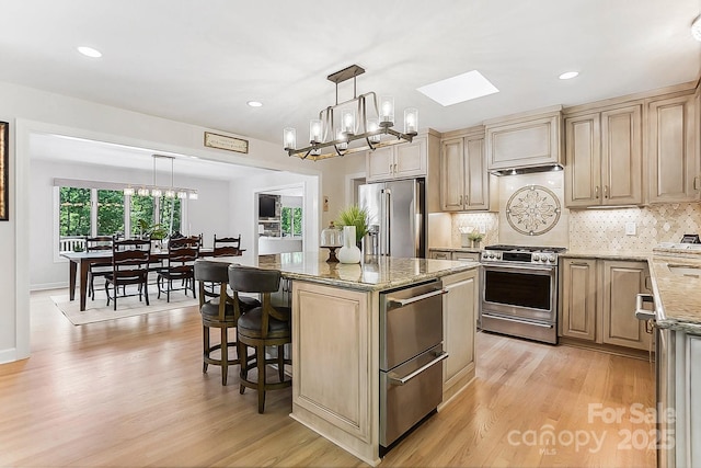 115 Forestcliff Ct NE, Concord, NC 28025 - kitchen with appliances with stainless steel finishes, a chandelier, light wood-type flooring, light stone counters, and a kitchen island