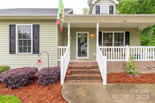 doorway to property with covered porch and a shingled roof