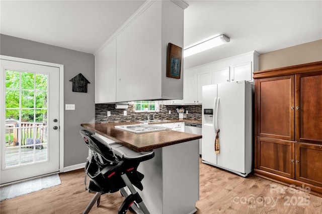 kitchen featuring dark countertops, light wood finished floors, white appliances, a peninsula, and backsplash