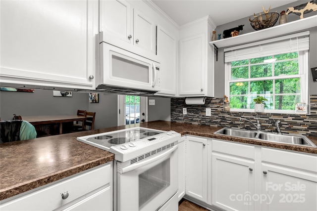 kitchen with a sink, dark countertops, white appliances, and white cabinetry