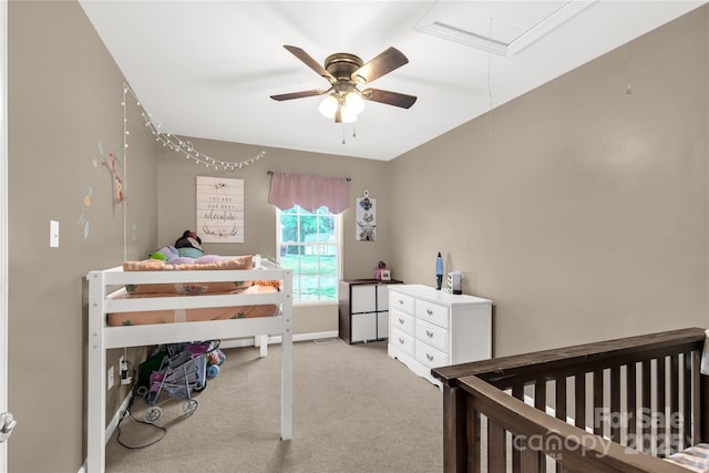 carpeted bedroom with a nursery area, baseboards, a ceiling fan, and attic access
