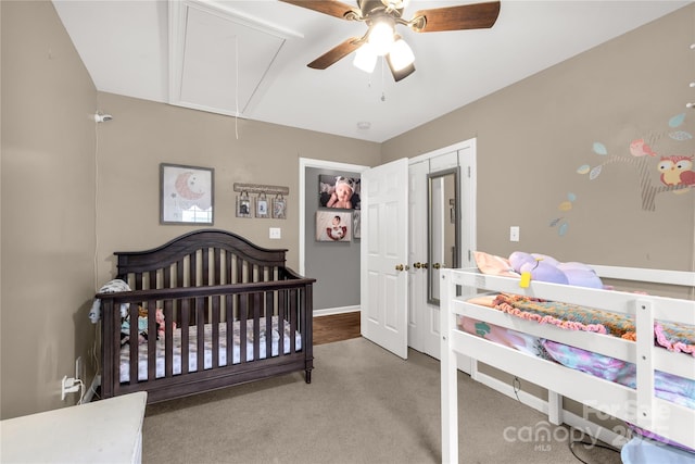 bedroom featuring a crib, ceiling fan, attic access, and carpet floors