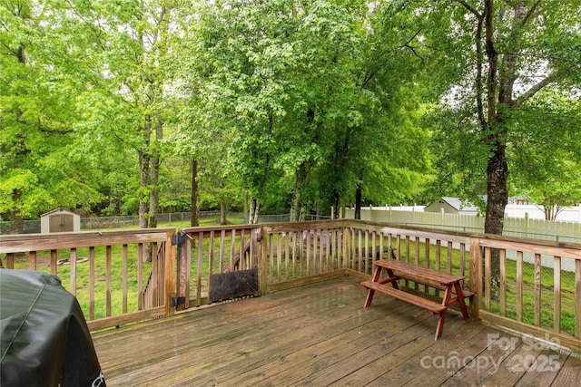 wooden deck featuring an outdoor structure, a fenced backyard, grilling area, and a storage shed