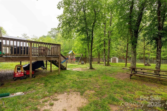 view of yard with a storage shed, an outbuilding, a wooden deck, a fenced backyard, and a playground