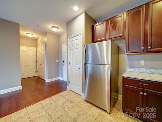 1000 E Woodlawn Rd Unit 402, Charlotte, NC 28209 - kitchen with light tile patterned floors, baseboards, freestanding refrigerator, and light stone counters