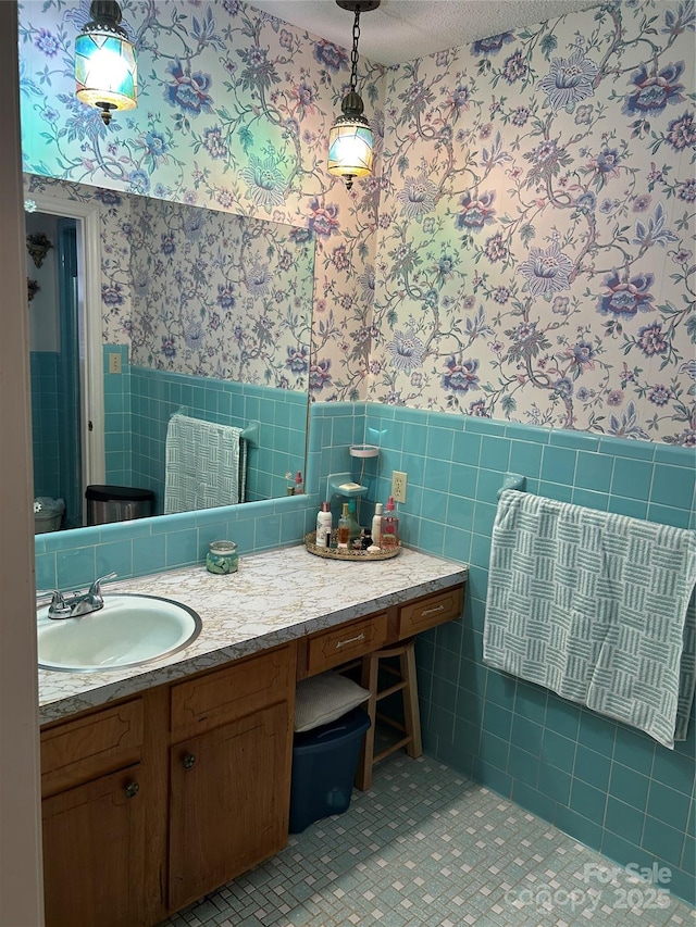 bathroom with tile walls, vanity, a textured ceiling, wainscoting, and wallpapered walls