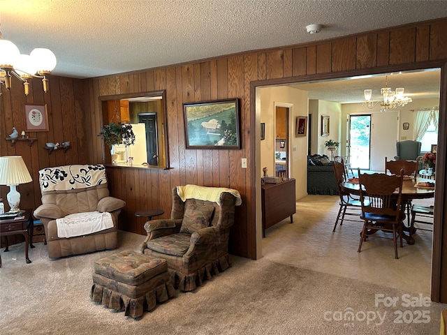 carpeted living room featuring a textured ceiling, wood walls, and a notable chandelier