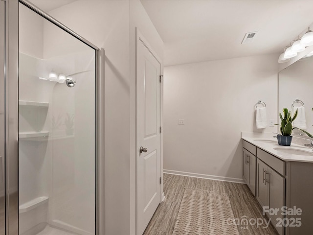 bathroom featuring double vanity, a shower stall, a sink, and wood finished floors