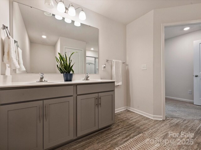 bathroom with double vanity, baseboards, a sink, and wood finished floors