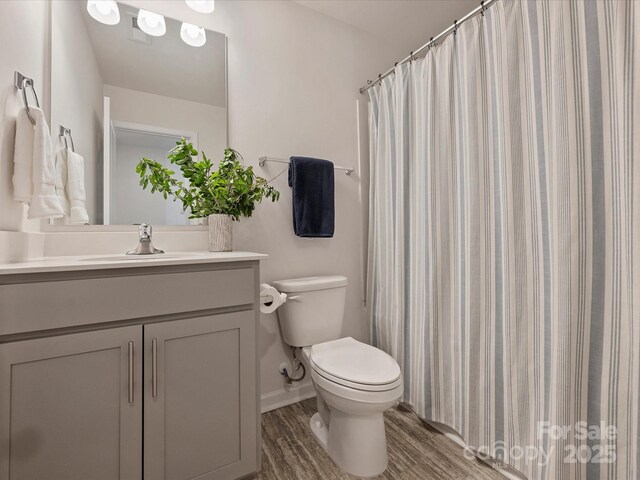 bathroom with a shower with curtain, wood finished floors, vanity, baseboards, and toilet