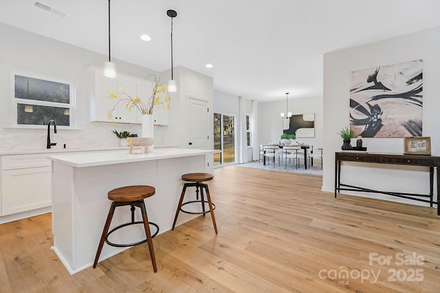 kitchen featuring white cabinets, a sink, light wood-style floors, backsplash, and visible vents