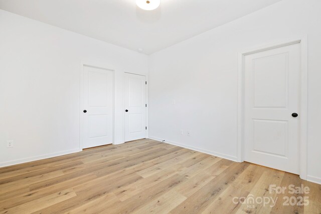 unfurnished bedroom with baseboards, light wood finished floors, and two closets