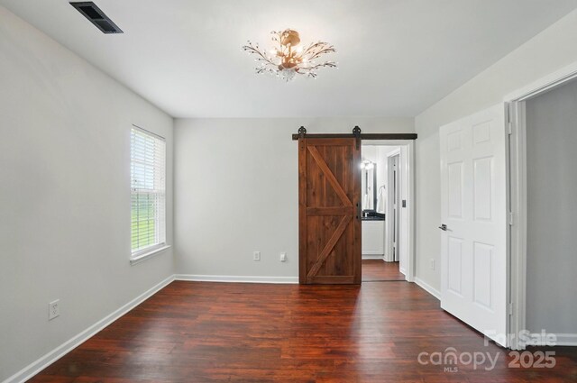 unfurnished bedroom with visible vents, a barn door, baseboards, and wood finished floors