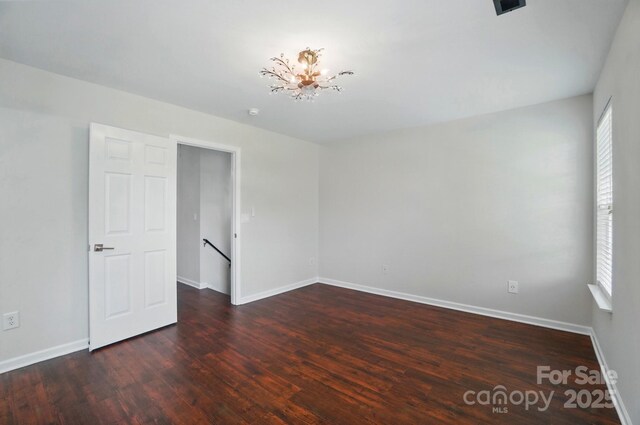 unfurnished room with baseboards, wood finished floors, and a notable chandelier