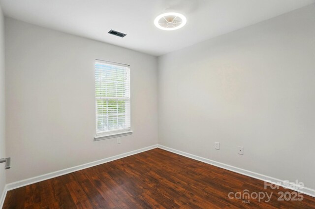 empty room featuring baseboards, visible vents, and dark wood-style floors