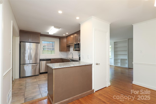 kitchen with appliances with stainless steel finishes, light stone countertops, a sink, a peninsula, and light wood-style flooring