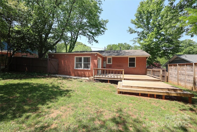 rear view of property featuring a lawn, brick siding, fence, and a wooden deck