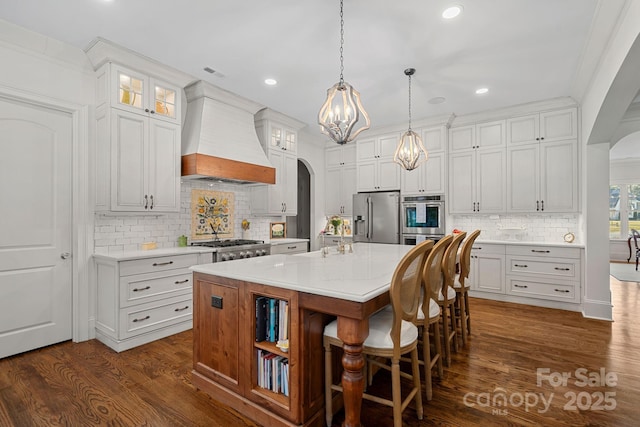 kitchen with dark wood-style flooring, a chandelier, stainless steel appliances, custom range hood, and arched walkways