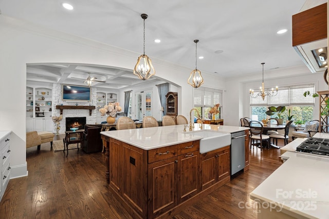 kitchen with appliances with stainless steel finishes, ceiling fan with notable chandelier, a stone fireplace, a sink, and ventilation hood