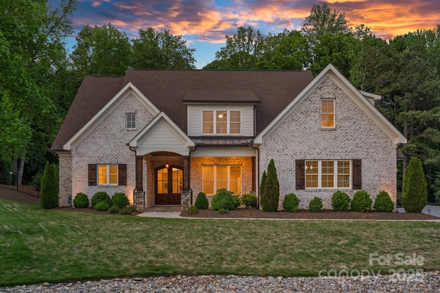 view of front of home featuring brick siding, french doors, a shingled roof, and a yard