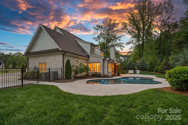 back of property with brick siding, fence, a yard, and a fenced in pool