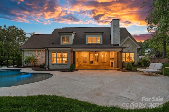 rear view of property featuring a chimney, brick siding, fence, a fenced in pool, and a patio