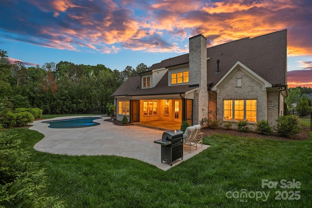 rear view of house with a chimney, brick siding, a patio, a lawn, and an outdoor pool