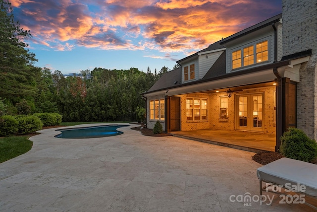 pool at dusk with a patio, a ceiling fan, an outdoor pool, and french doors