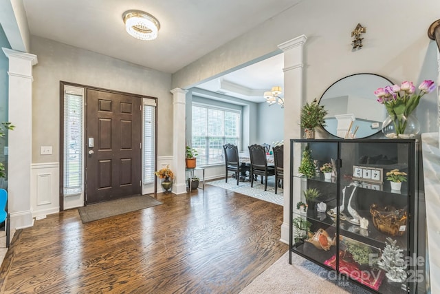 entrance foyer with wood finished floors, a decorative wall, and decorative columns