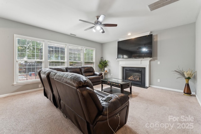 carpeted living area featuring baseboards, a fireplace with flush hearth, a ceiling fan, and visible vents