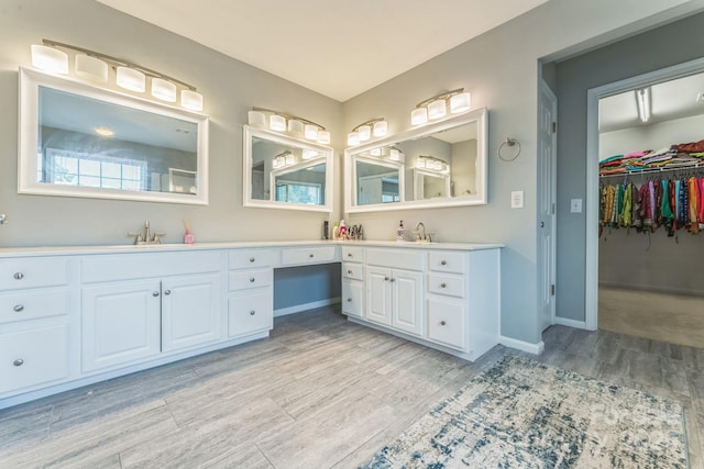 bathroom featuring a walk in closet, baseboards, wood finished floors, and vanity