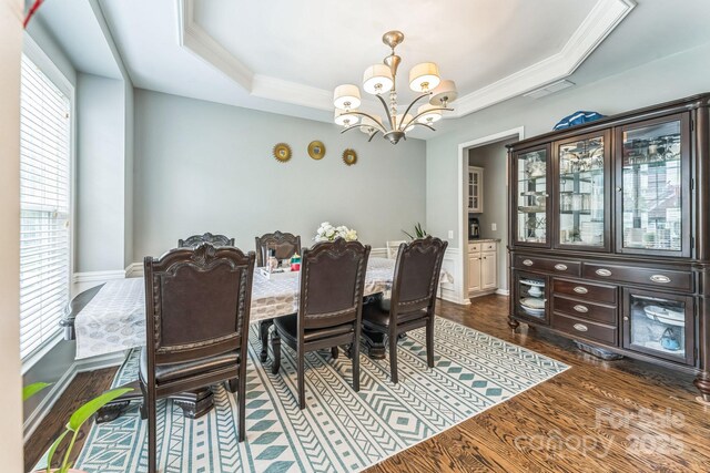 dining area featuring dark wood-style flooring, visible vents, a chandelier, crown molding, and a raised ceiling