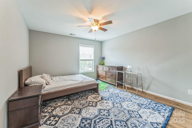 bedroom featuring baseboards, a ceiling fan, visible vents, and wood finished floors