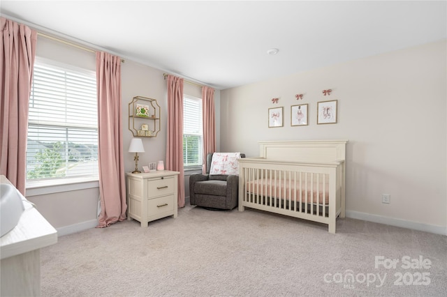 bedroom with baseboards, a nursery area, and light colored carpet
