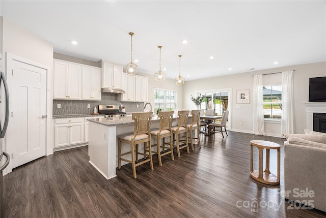 kitchen featuring a kitchen bar, gas range, dark wood finished floors, under cabinet range hood, and an island with sink