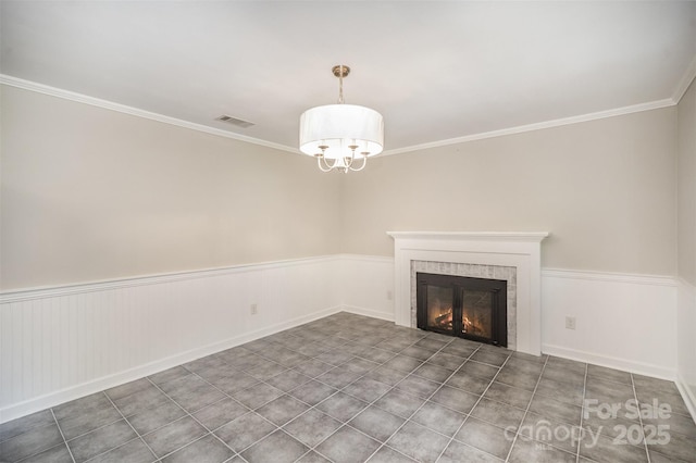 unfurnished living room featuring a fireplace, crown molding, a wainscoted wall, a chandelier, and baseboards