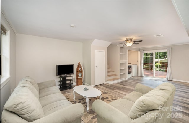 living area featuring light wood-type flooring, stairway, baseboards, a ceiling fan, and washer / clothes dryer