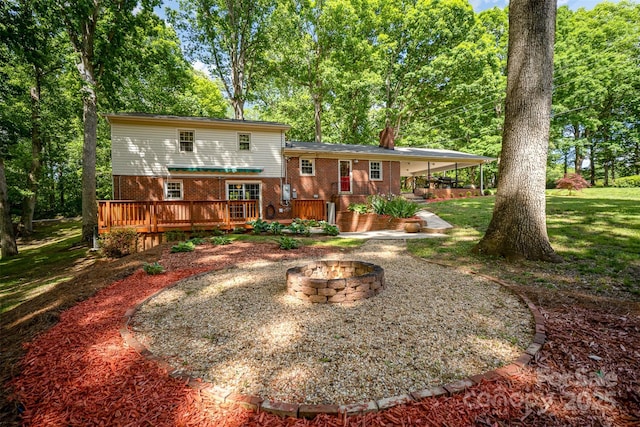 rear view of house featuring a fire pit, brick siding, a wooden deck, and a yard