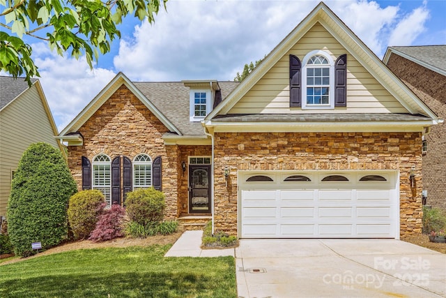 view of front of home featuring a shingled roof, stone siding, concrete driveway, and a front yard
