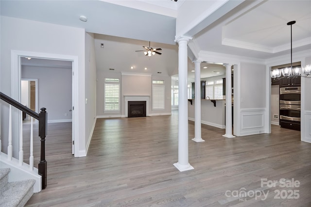 unfurnished living room featuring ceiling fan, stairway, crown molding, a fireplace with flush hearth, and light wood finished floors