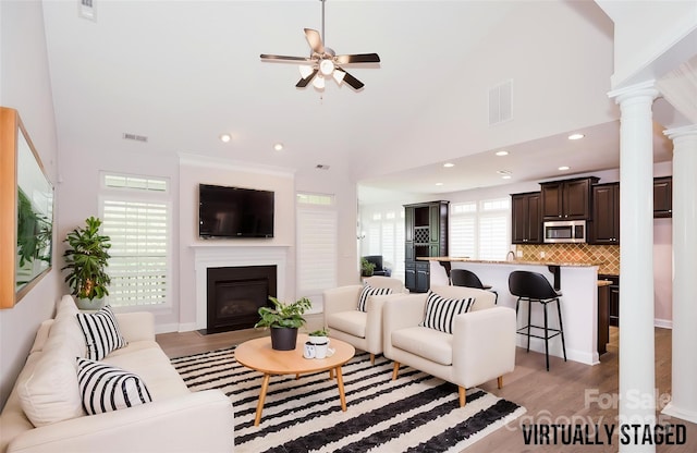 living area with a ceiling fan, a fireplace with flush hearth, recessed lighting, light wood-type flooring, and decorative columns