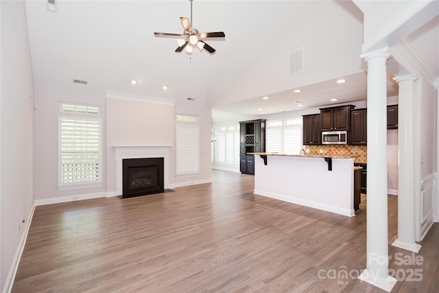 unfurnished living room featuring ceiling fan, ornate columns, a fireplace with flush hearth, light wood finished floors, and recessed lighting