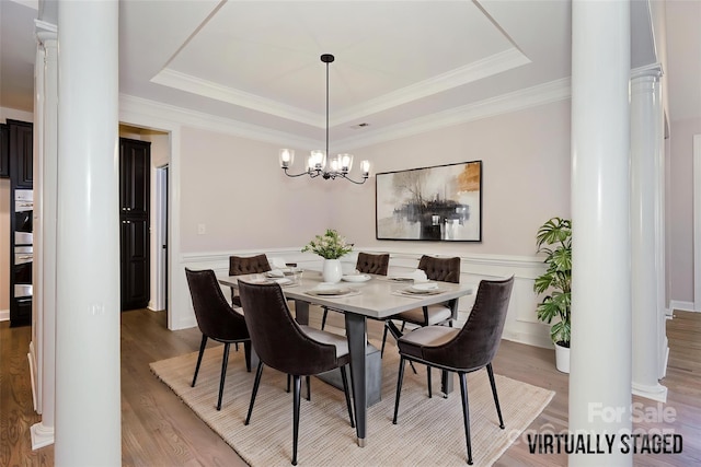 dining room featuring ornate columns, a tray ceiling, a chandelier, light wood-style floors, and a wainscoted wall
