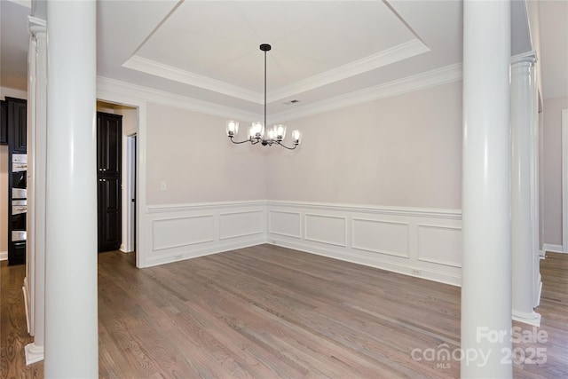 unfurnished dining area with decorative columns, a raised ceiling, wood finished floors, wainscoting, and ornamental molding