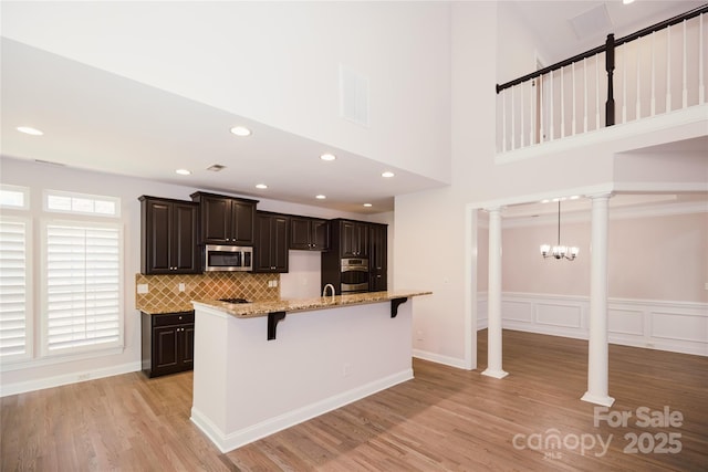kitchen featuring appliances with stainless steel finishes, a kitchen breakfast bar, ornate columns, light wood-type flooring, and a towering ceiling