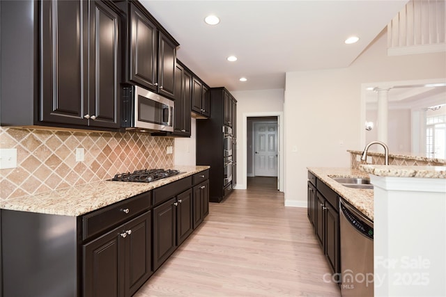 kitchen featuring stainless steel appliances, a sink, light wood-style flooring, decorative backsplash, and light stone countertops