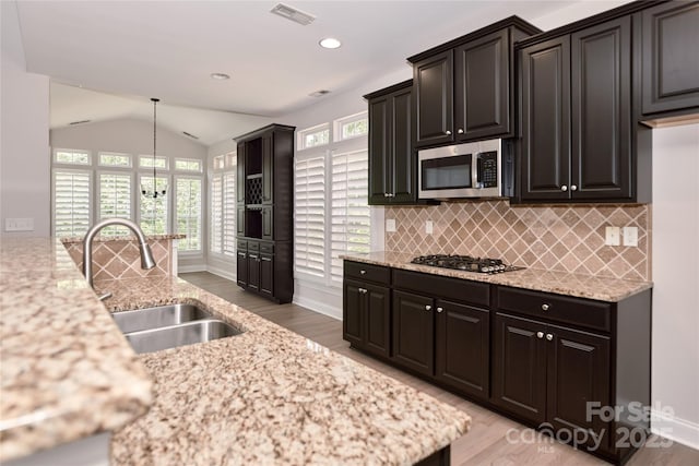 kitchen featuring a sink, stainless steel appliances, light wood-style floors, lofted ceiling, and tasteful backsplash