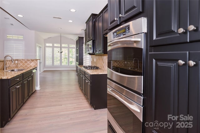 kitchen featuring a sink, light wood-style floors, decorative backsplash, light stone countertops, and appliances with stainless steel finishes