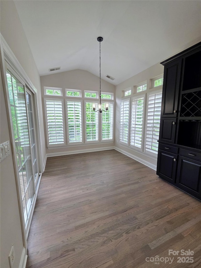 unfurnished dining area featuring a chandelier, vaulted ceiling, wood finished floors, and baseboards
